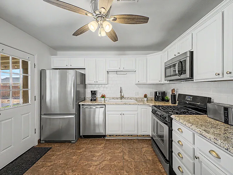 Efficient kitchen with ample white cabinetry, granite counters, subway tile backsplash, and stainless steel appliances.