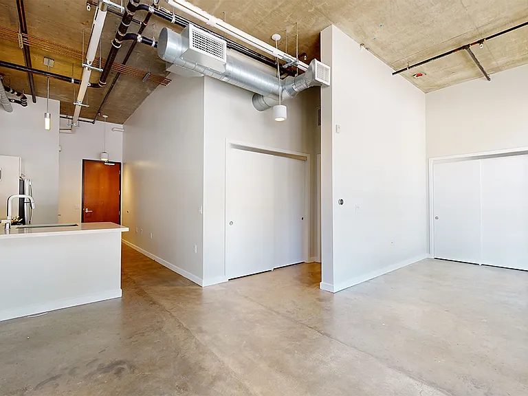 Apartment kitchen with stainless steel appliances, dining and living room with polished concrete flooring.