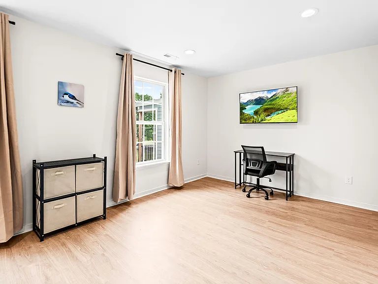 Spacious room with wood-look flooring, large windows with drapes, and a built-in work area ideal for studying or WFH.