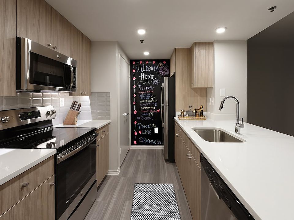 Renovated Package II kitchen with white quartz countertops, white tile backsplash, driftwood cabinetry, stainless steel appliances, and hard surface plank flooring