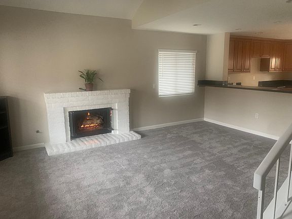 View of living room from entry. Gas fireplace with cable-ready wiring above. Open view to kitchen with bar-seating area between.