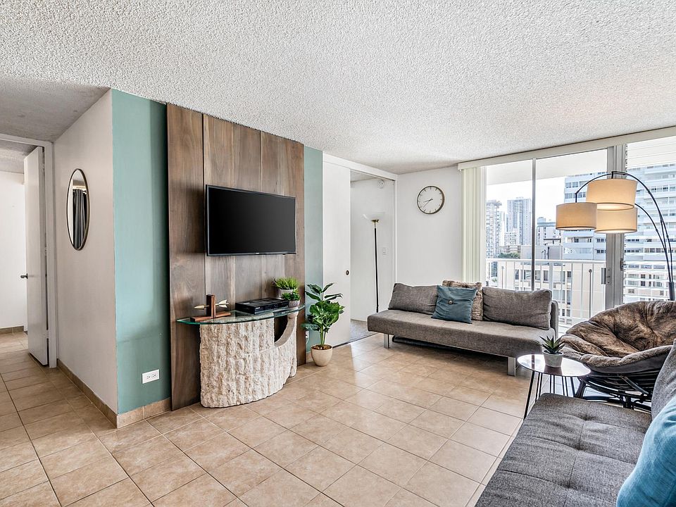 living room with 2 large couches, lounge chair, pillows, art work, lamps and TV. Slider to lanai. View of living room to see slider door to one bedroom and hallway to additional bedroom and bathrooms