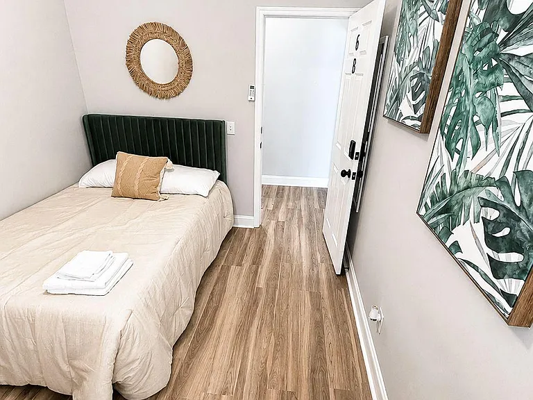 Private bedroom with wood-look flooring, high transom window, and a comfortable bed setup with wall decor.