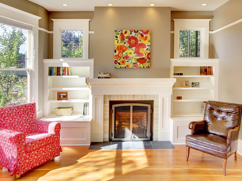 Bright, south-facing living room with bay windows, built-ins, and gas fireplace. Warm recessed lighting throughout.