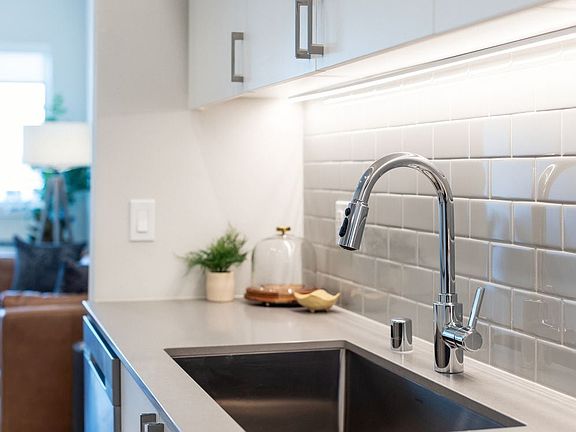 Kitchen with grey quartz countertops, white cabinetry, and grey subway tile backsplash