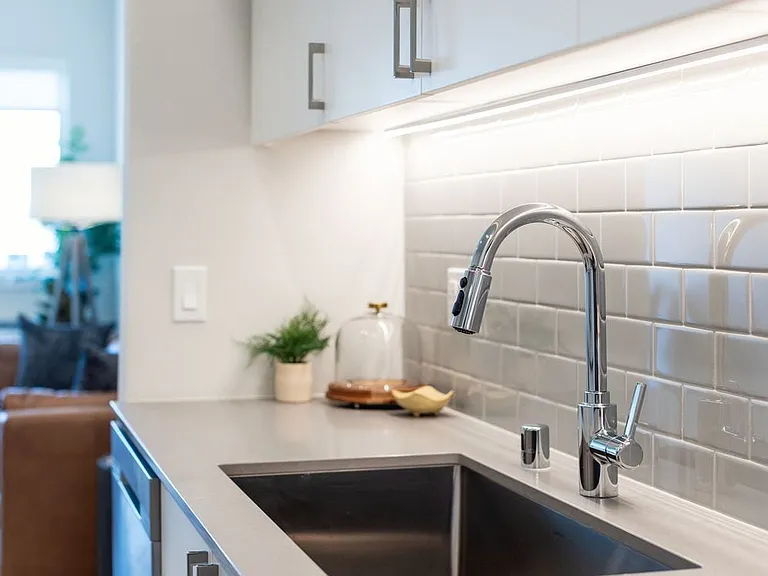 Kitchen with grey quartz countertops, white cabinetry, and grey subway tile backsplash