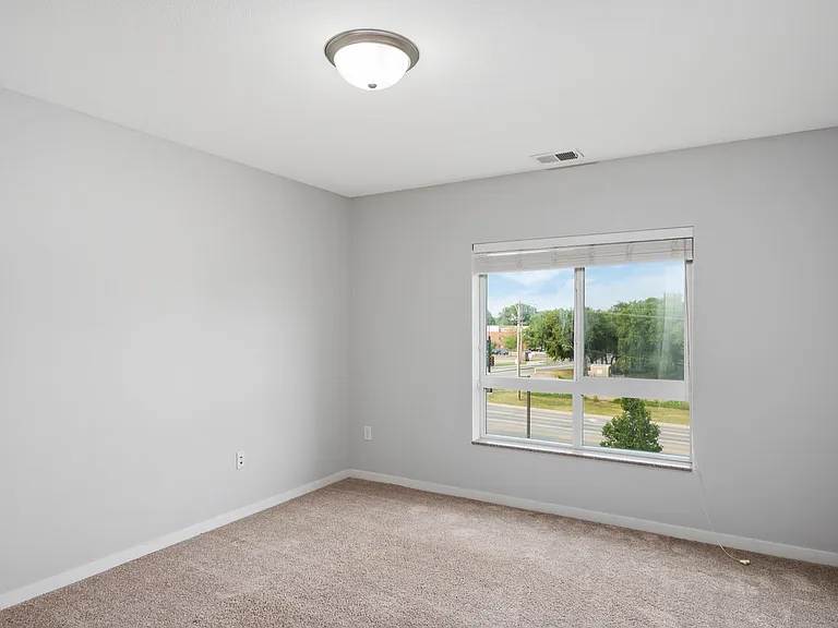 Bright, minimalist bedroom space featuring fresh carpeting and a large window with scenic outdoor views. Bright, minimalist bedroom space featuring fresh carpeting and a large window with scenic outdoor views.