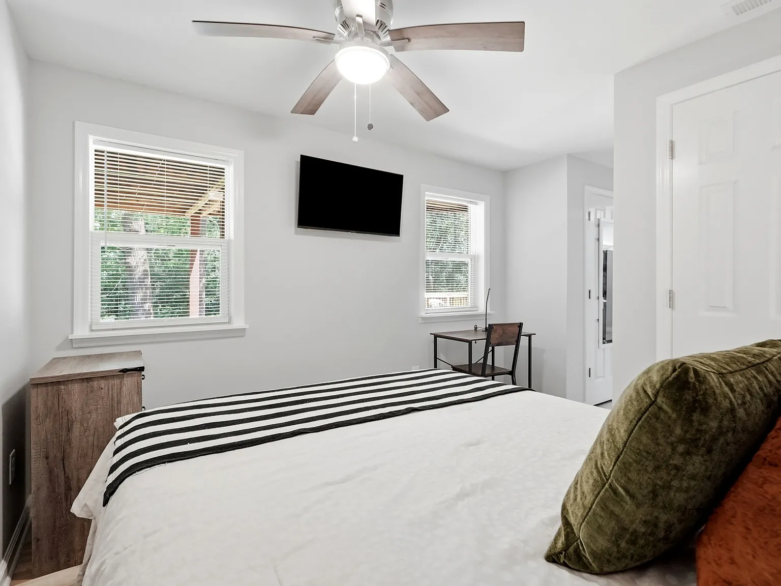 Fully furnished private suite with Smart TV, workspace, natural light, and comfortable sleeping space.