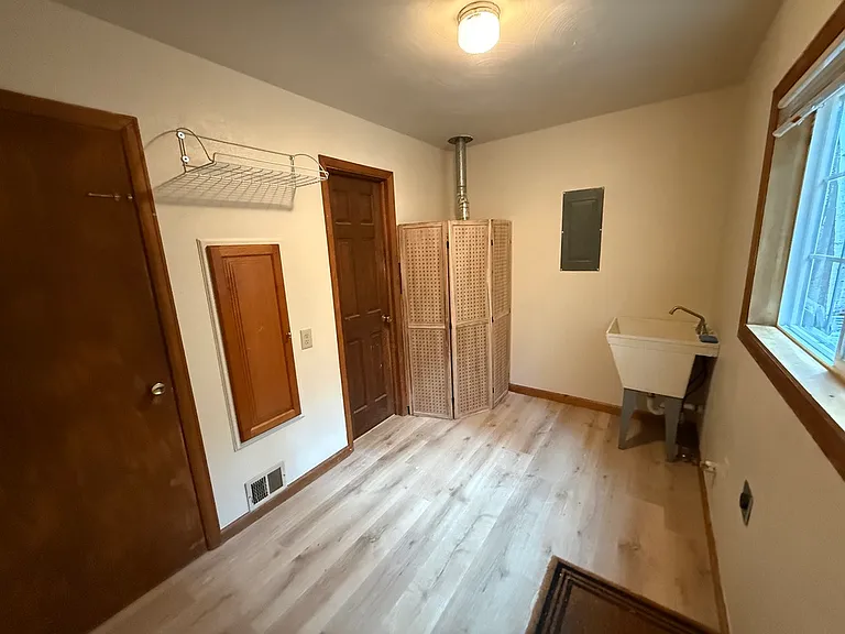Utility room (taken from back door). Left to right: furnace closet, extra wall cabinet and shelf, door to bathroom, enclosed hot water heater and water filter, laundry tub, space for washer/dryer