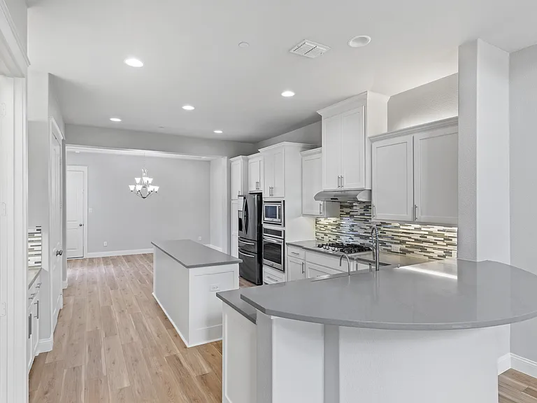 Gourmet kitchen, featuring quartz countertops and island, stainless steel appliances including a refrigerator, a gas cooktop, a Paragon water system, and abundant wood cabinetry.