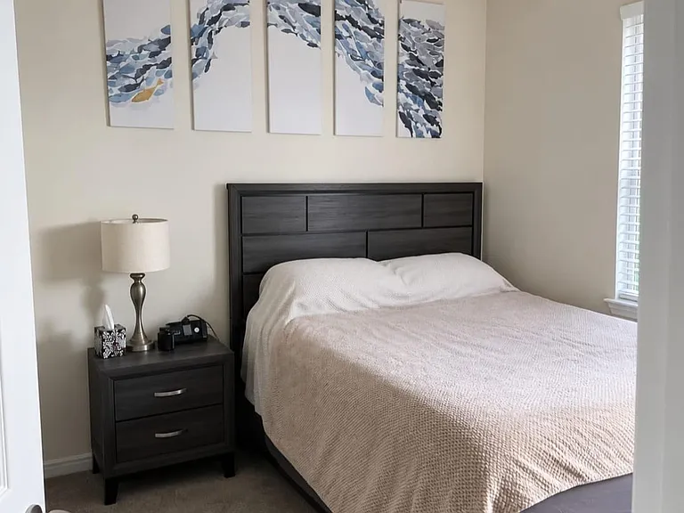 Well-appointed bedroom featuring a full bed, matching nightstand with lamp, and a window with blinds for natural light.
