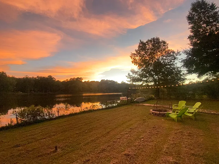 Backyard under the sunset with firepit, seating, dock access, and string lighting.
