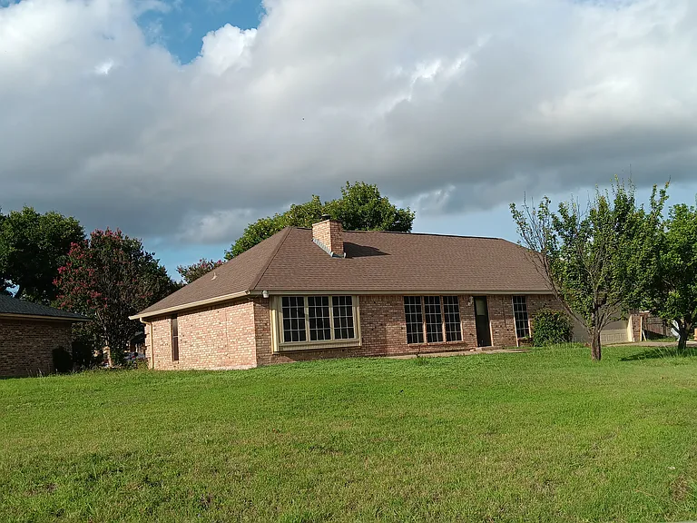 Back side photo of house before fence installation. showing solar screen, patio with ramp and two car garage with garage door opener. Fruit bearing trees . A little of country in the city.