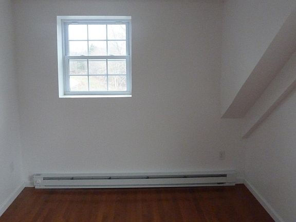 View of the bright bedroom, has two windows - one that is on the right side. Fits a queen bed with a dresser and side table.