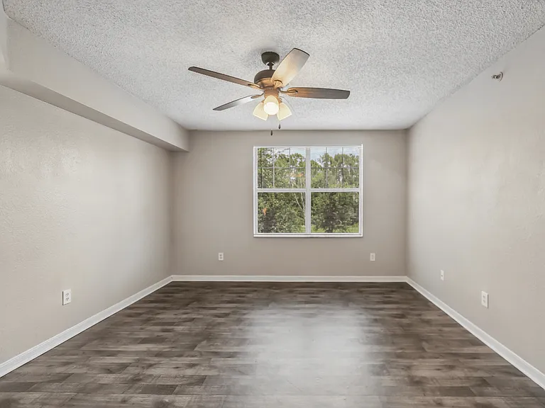Bright living room with large window, wood-style flooring, and ceiling fan in a 1-bedroom apartment at Gregory Cove in Jacksonville, FL.