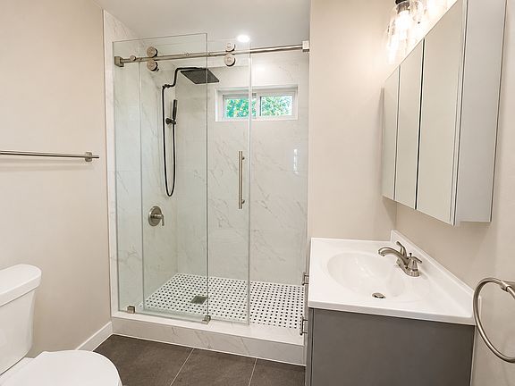Fully renovated bathroom featuring marble-look shower tile, glass shower door, updated vanity, modern fixtures, and fresh finishes.