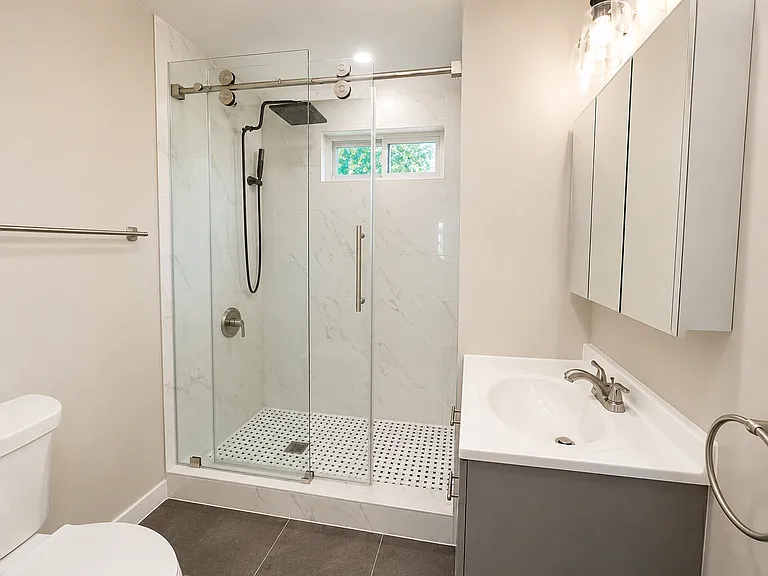 Fully renovated bathroom featuring marble-look shower tile, glass shower door, updated vanity, modern fixtures, and fresh finishes.