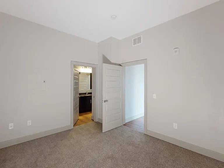 Spacious apartment bedroom with attached bathroom and plush carpet flooring.