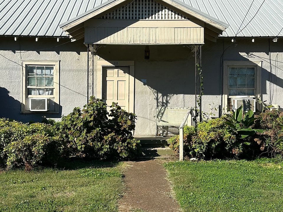 View of concrete front porch with wrought iron bench and table.