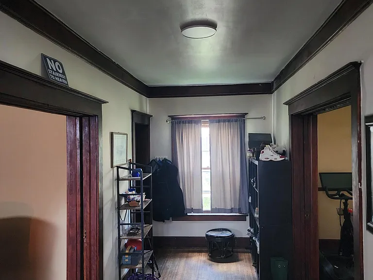 Hall area between living area spaces. Front hallway and front door access. Stairs right behind.