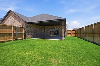 A backyard with green grass, a covered patio, and a fenced wooden fence surrounding a brick house un