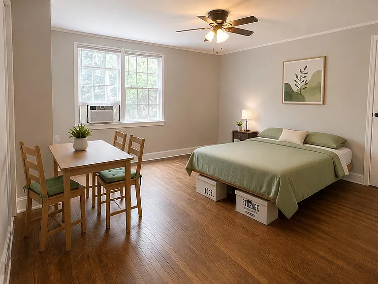 Spacious furnished bedroom featuring hardwood floors, a work/dining table set, and a window A/C for added comfort.