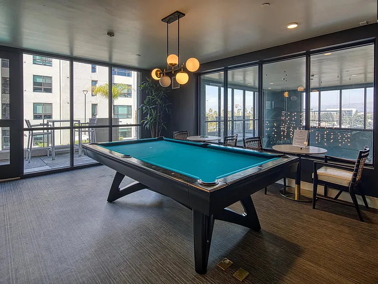 Game lounge with a pool table, bar seating, and large windows offering open views of the surrounding community.