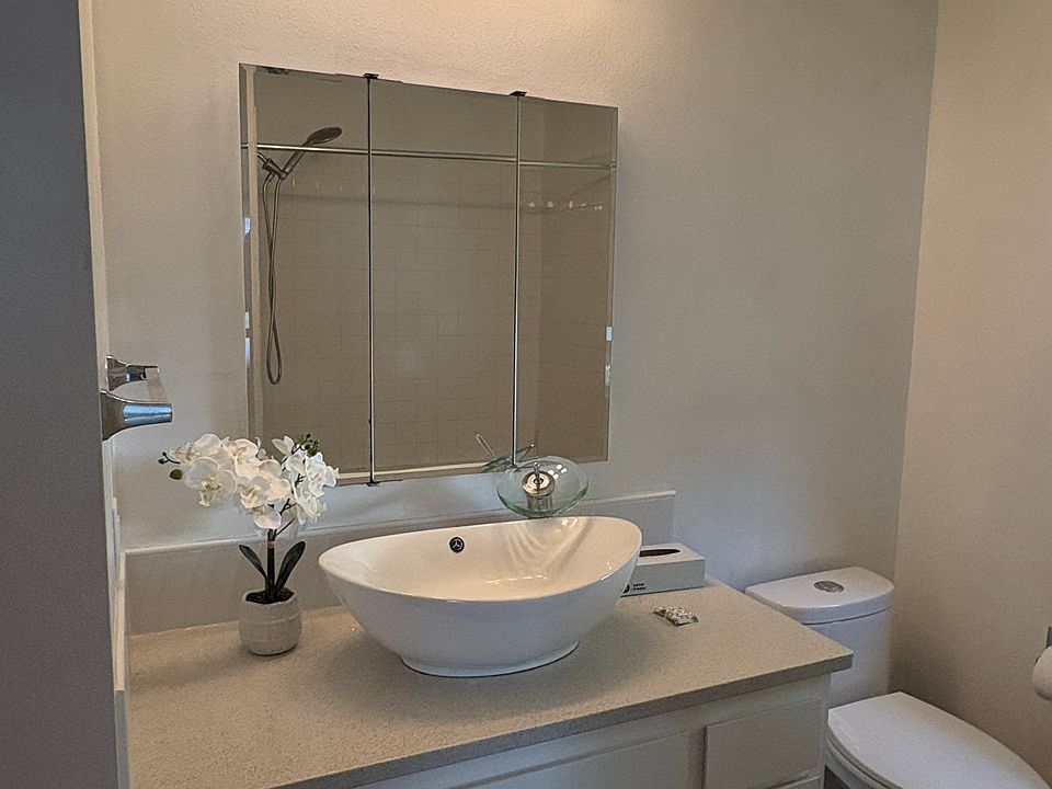 Primary suite bath. Vessel sink, waterfall faucet, mirrored medicine cabinet, quartz counter, tile floor& water saving dual flush toilet. Connecting door to hall for guest access.