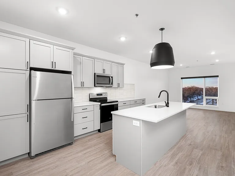 Modern open-concept kitchen with sleek gray cabinets, stainless steel appliances, and a stylish island overlooking a bright living area with large windows. Modern open-concept kitchen with sleek gray cabinets, stainless steel appliances, and a stylish isl