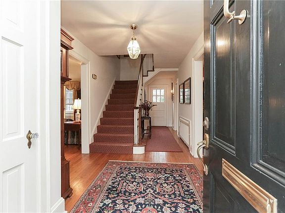 Oversized front door with Williamsburg brass door knocker and huge brass lock and key on the inside frame the large entrance foyer with shiny oak floors lead back to formal steps ,powder room and back door.