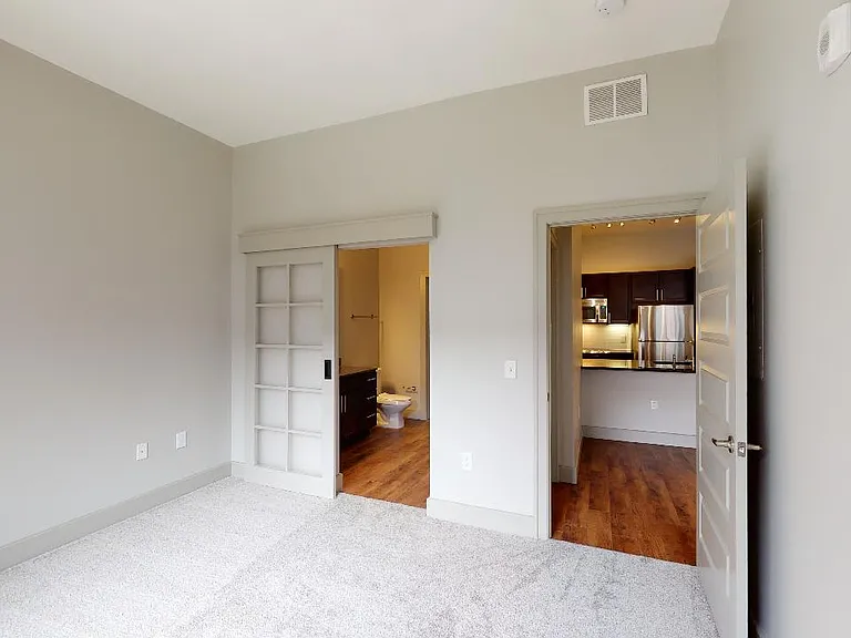 Spacious apartment bedroom with attached bathroom and plush carpet flooring.