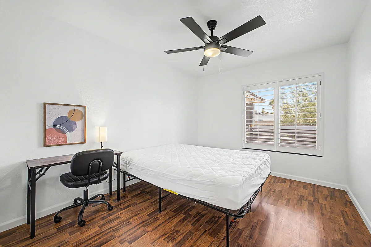 Private bedroom with ceiling fan, wood-look flooring, and a workstation; plantation shutters provide privacy and daylight. - E Tierra Buena Ln