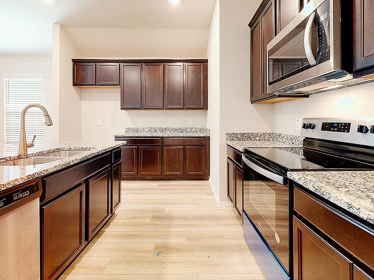 Well-appointed kitchen featuring granite countertops, stainless-steel appliances, ample dark-wood cabinetry, and a center island with breakfast-bar seating _ open to the family room.