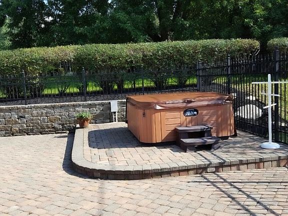Six person hot tub in the pool area which is enclosed with black aluminum fencing and 1600 sq ft brick pavers.