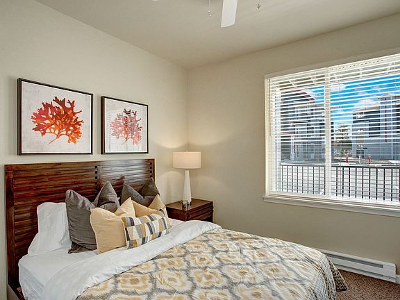 A bedroom with a large window looking out to the patio and the rest of the property with a bed, nightstand, and ceiling fan