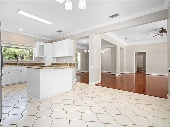 Kitchen featuring light wood-type flooring, ceiling fan with notable chandelier, white cabinets, ornamental molding, and stainless steel fridge