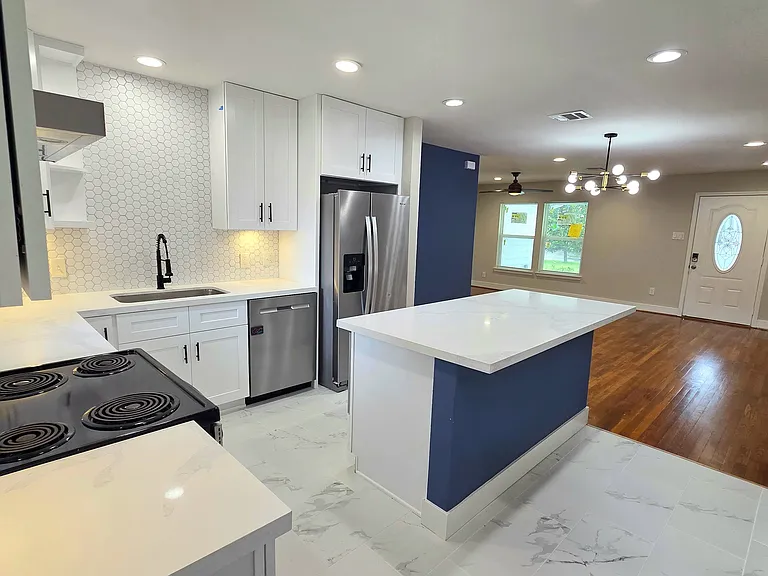 Spacious open-concept kitchen and living area. The kitchen features white cabinetry, a tile backsplash, stainless steel appliances, and an island. The space creates a bright and inviting atmosphere.