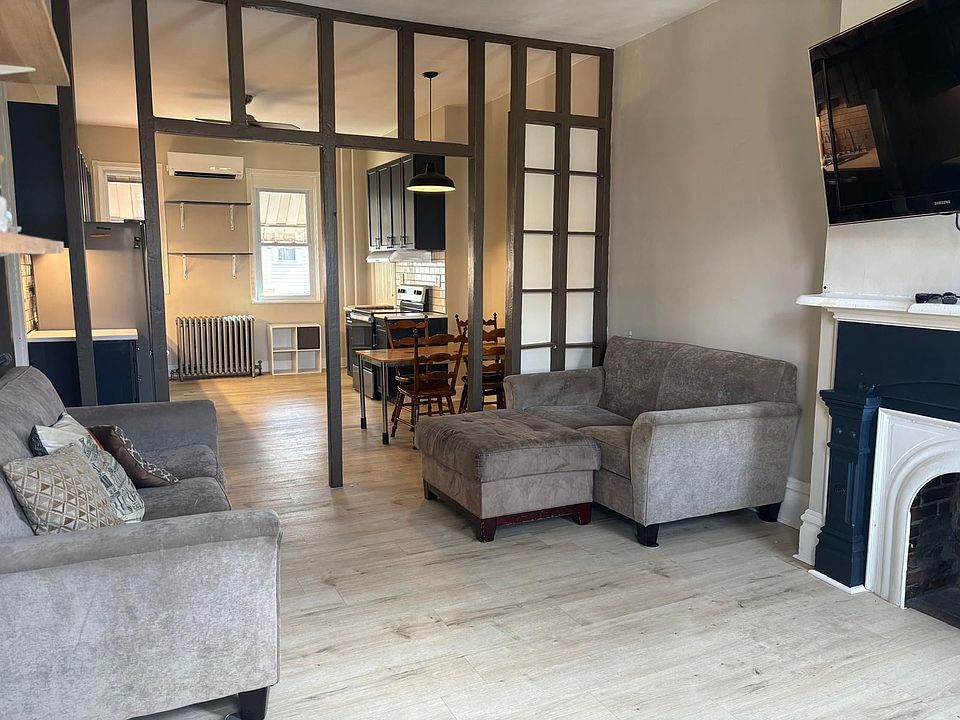 Livingroom featuring (non-functional) fireplace, built in adjustable shelving, windows looking out the front of the house, ceiling fan, and closet. Couches and TV included
