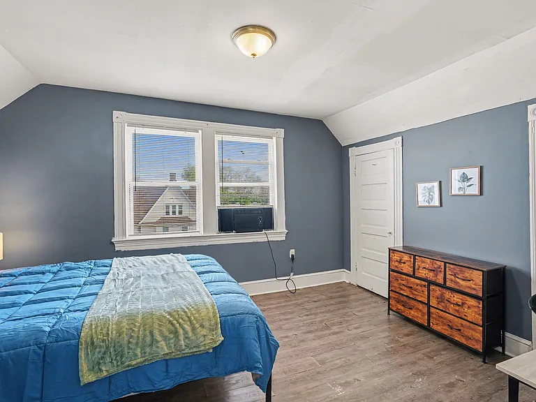 Private bedroom with a large window, wood-look flooring, and space for a bed plus dresser and work area.