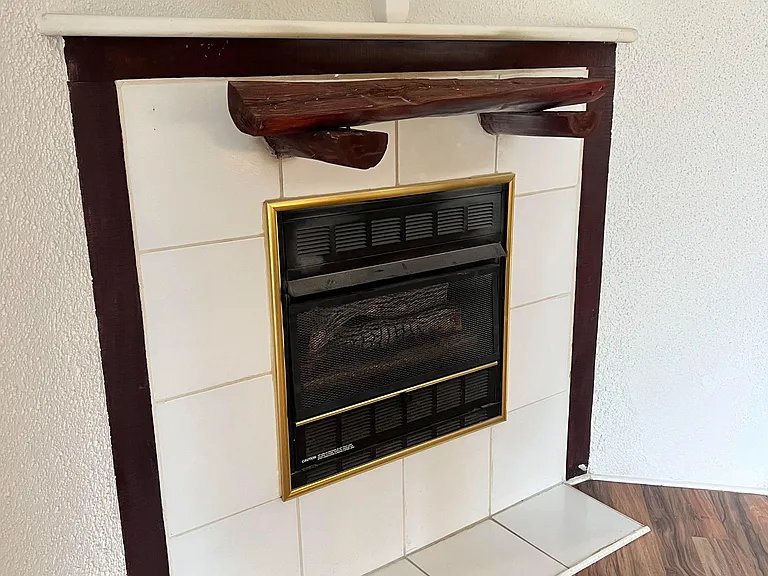 Corner fireplace with tiled surround and wood mantel adds a functional focal point to the main living area.