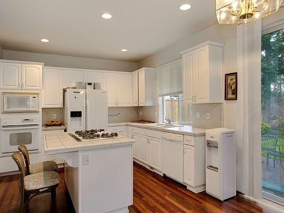 Spacious kitchen with tile counters and large island with 5 gas burners. Kitchen has dining area with sliders to patio.