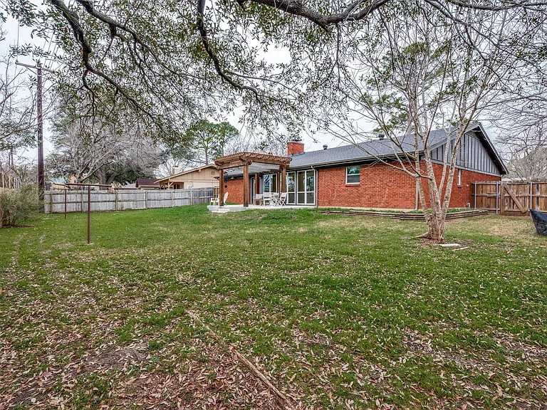 Expansive backyard with a manicured lawn, brick exterior, wood fence, and a patio featuring a pergola
