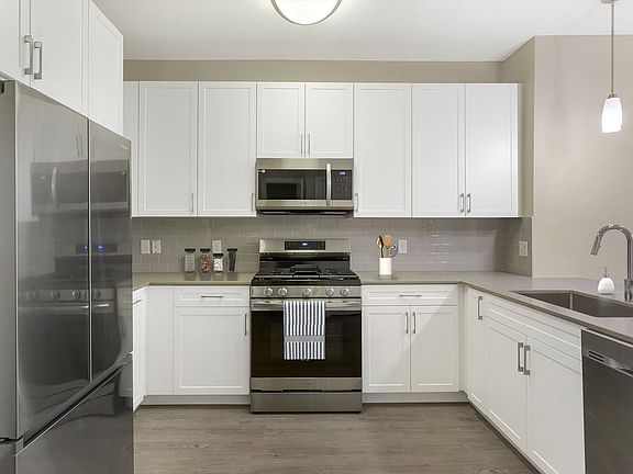 Renovated Package II kitchen with grey quartz countertops, white cabinetry, grey tile backsplash, stainless steel appliances, and hard surface flooring