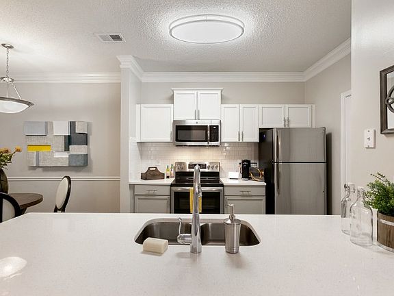 Interior photo of the kitchen with stainless steel appliances, white subway tile, blue cabinets and laundry room
