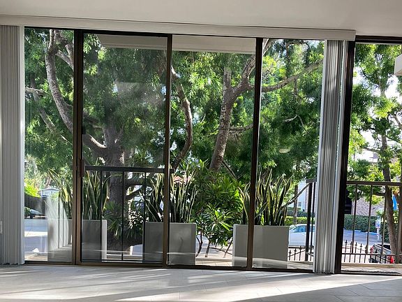 Bright, airy, open concept front room/dining nook view downtown La Jolla's upper Cave St. through floor-to-ceiling sliding door and a sea of green Snake plants and Podocarpus trees.