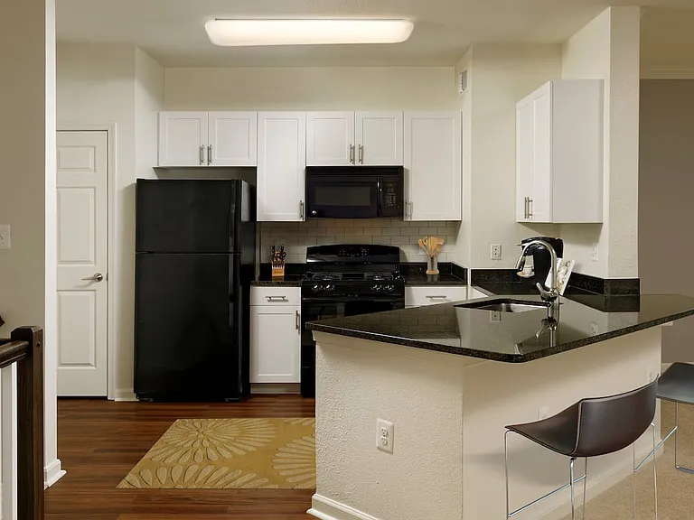 Renovated Package II kitchen with white cabinetry, black granite countertops, black appliances, white tile backsplash, and hard surface plank flooring