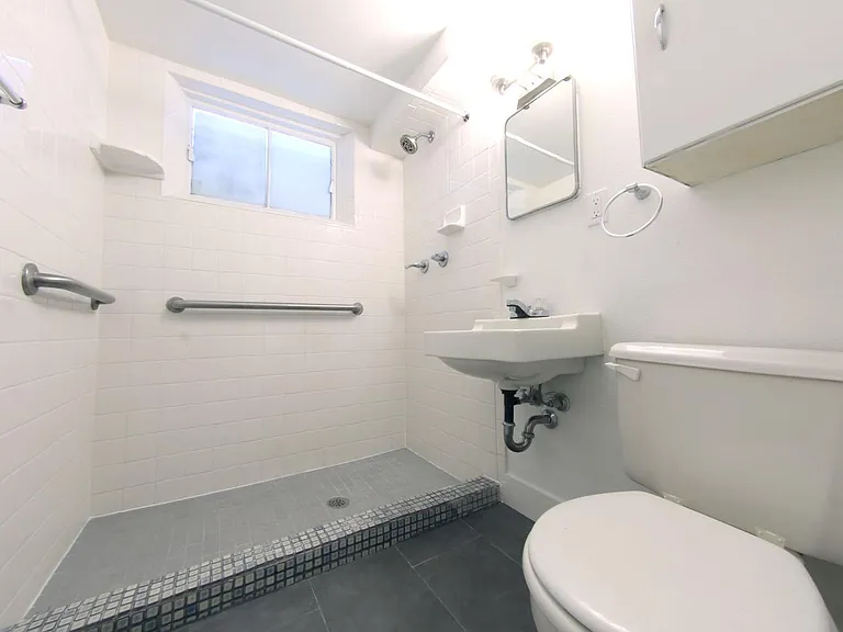 Basement bathroom with large shower, new slate tile floor, and ample storage.