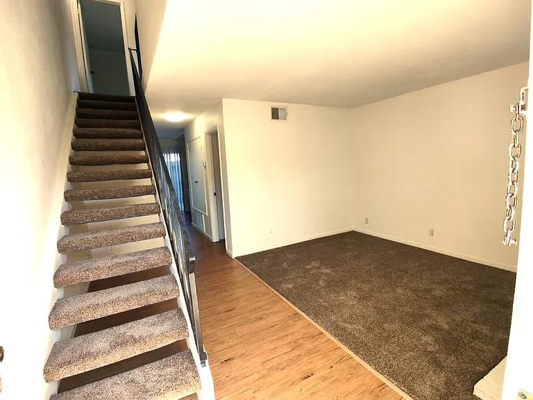 Wonky photo from the perspective of the front door, showing stairs up, and living room.