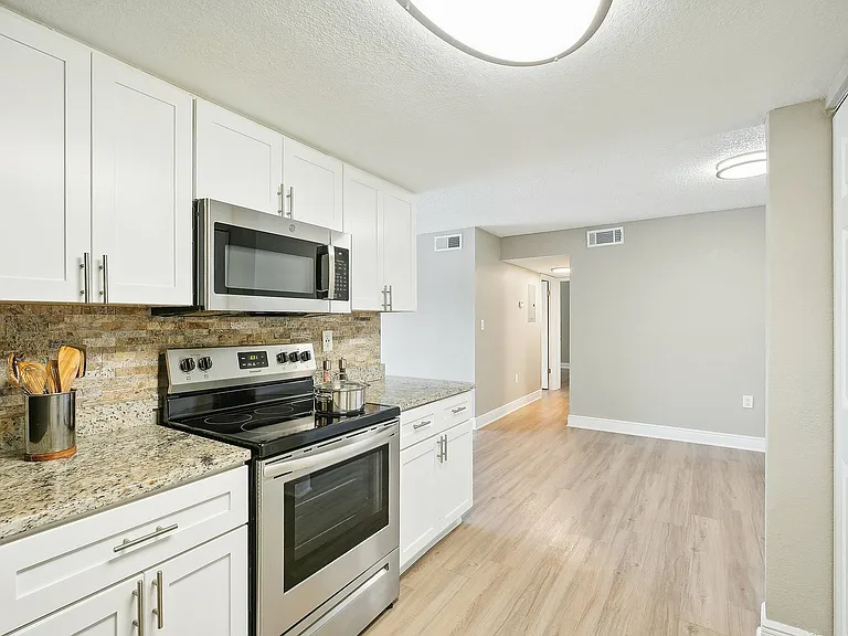 Modern kitchen with granite countertops, stainless steel appliances, and elegant cabinetry in a spacious apartment.