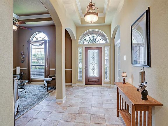 Light and bright Entry: Mahogany front door with 3/4 leaded and beveled glass, transom and arched windows, tray ceiling, and neutral tile floors.